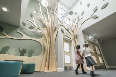 Sculpture in form of two trees. Two children holding hands walk under trees in school reception area.